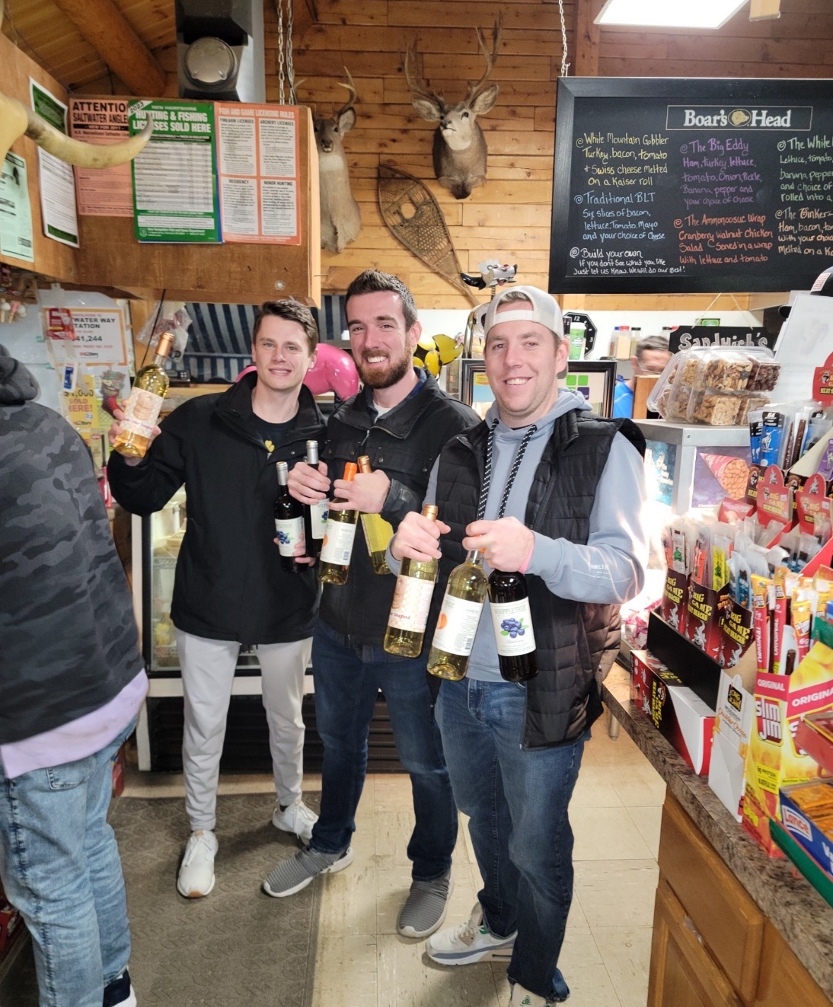 Customers showing off wine bottles at the counter with Boars Head menu